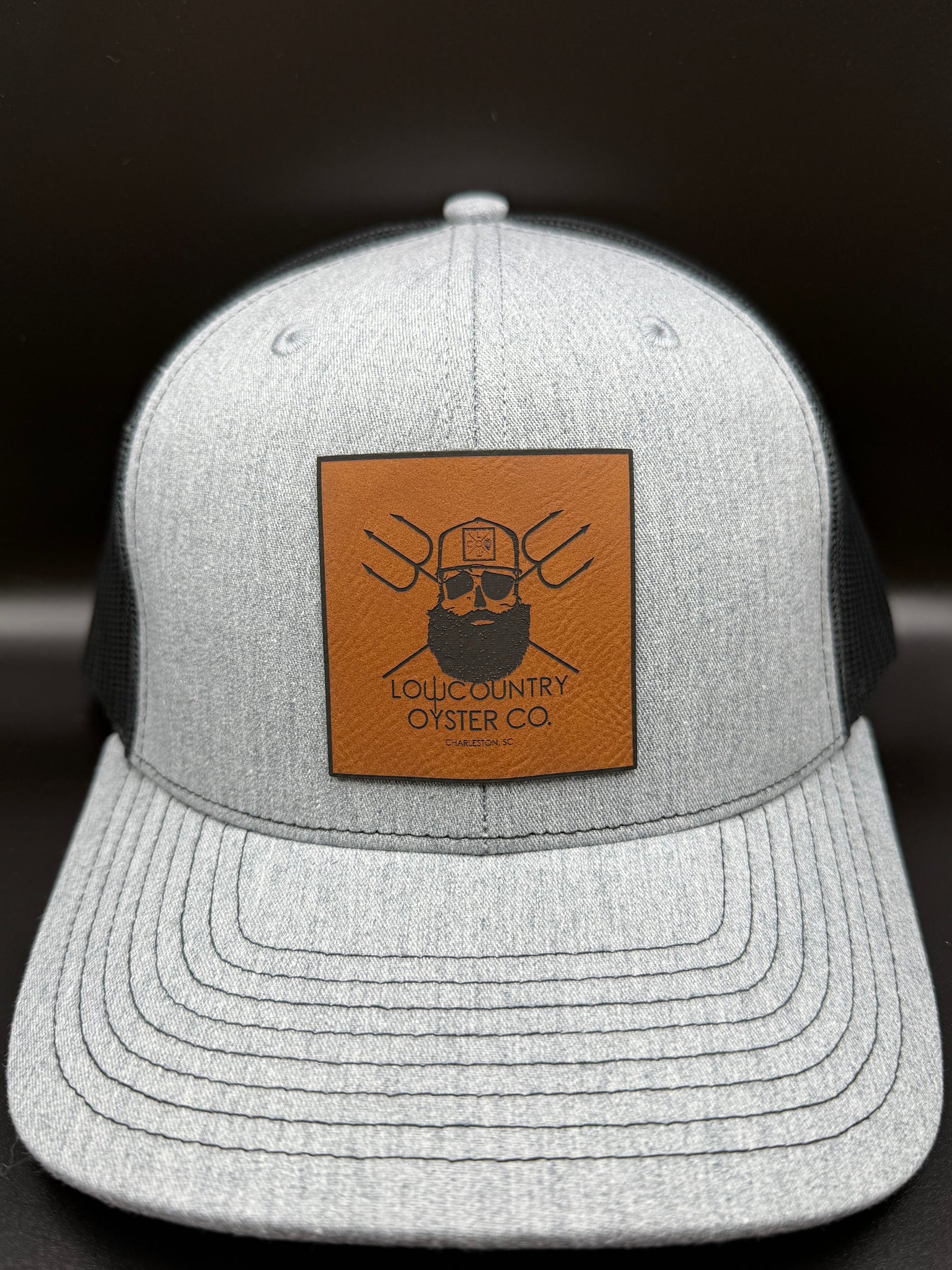 Gray cap with a brown leather patch featuring a logo and text on a black background
