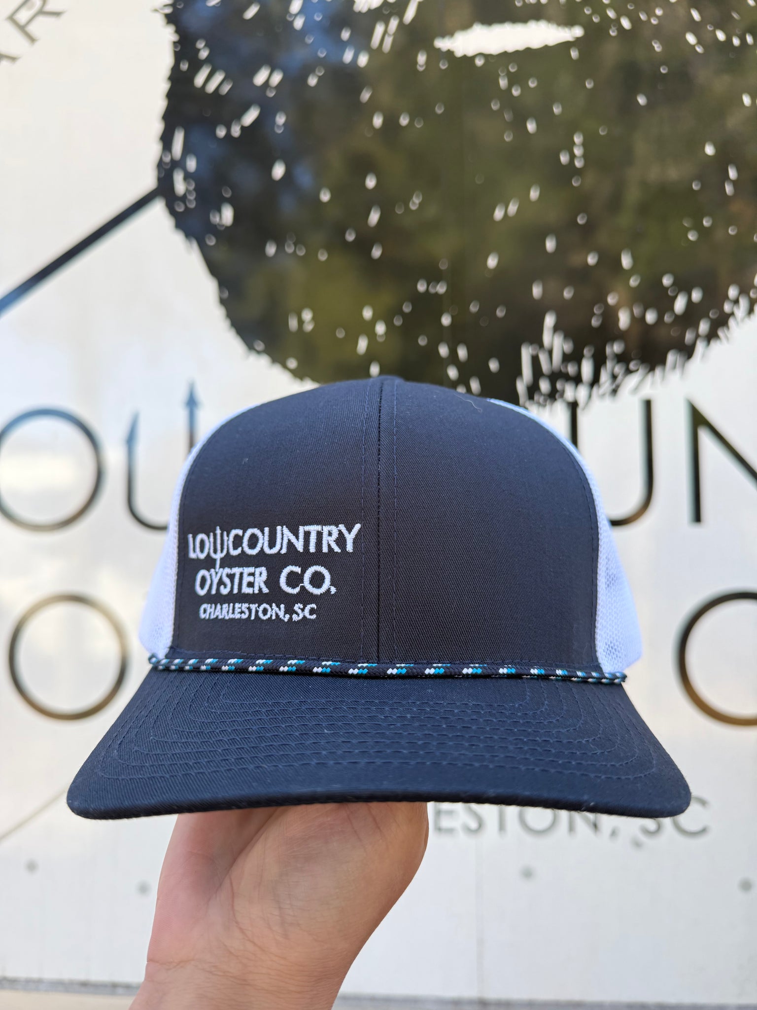 Blue and white cap with 'Lowcountry Oyster Co.' text held in front of a branded background.